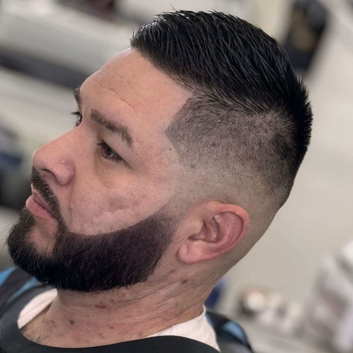 High skin fade with a sharp part and a shaped full beard, cut at Tu Barber Cubanito in Brighton, Colorado